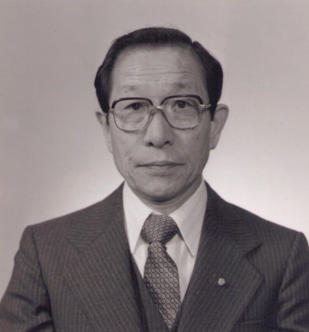 A portrait of Principal Shuyu Kurai in a pinstripe suit and glasses