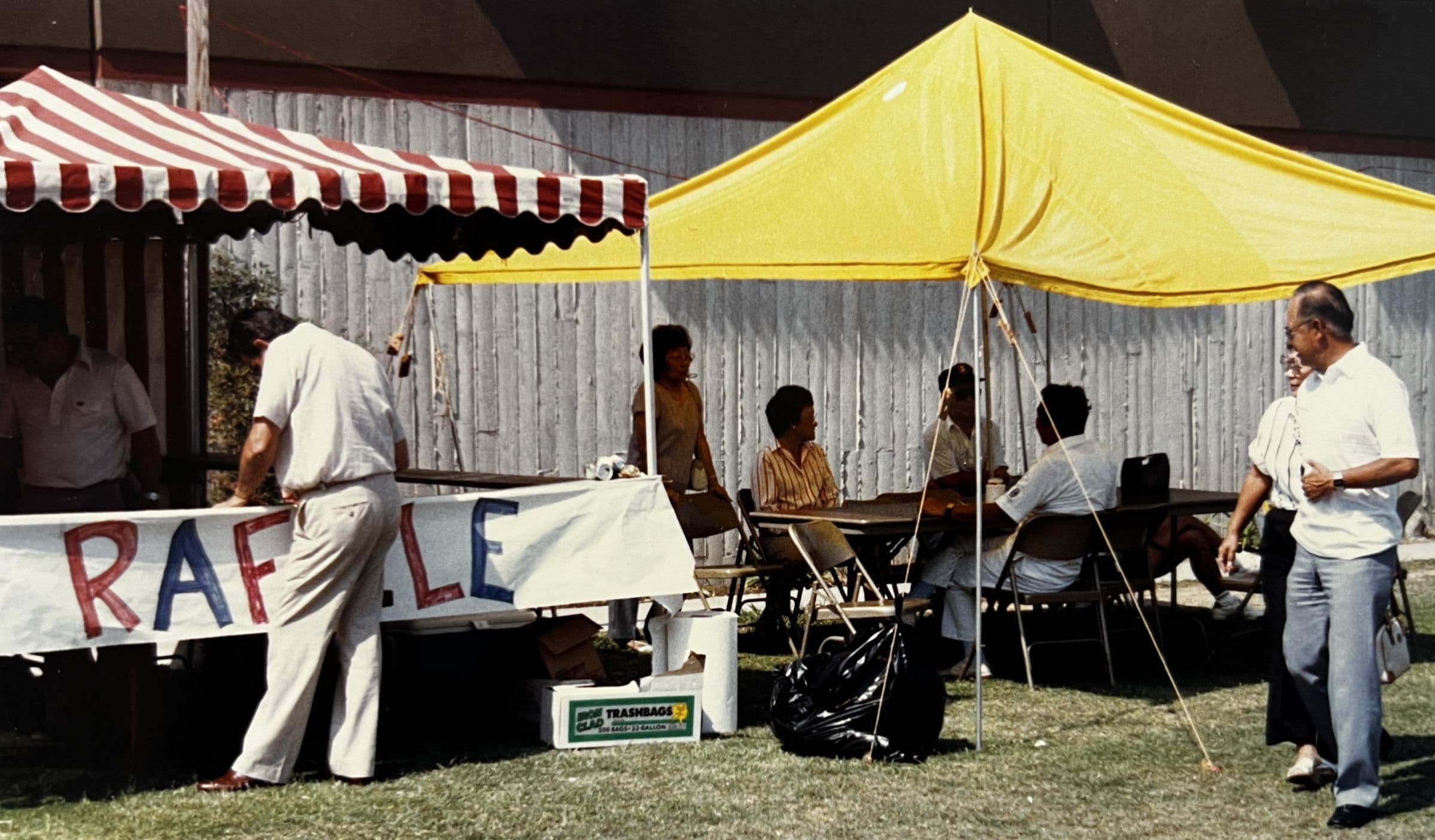 Volunteers running a hand-lettered raffle booth under striped and yellow tents on the center's lawn at the 1988 festival