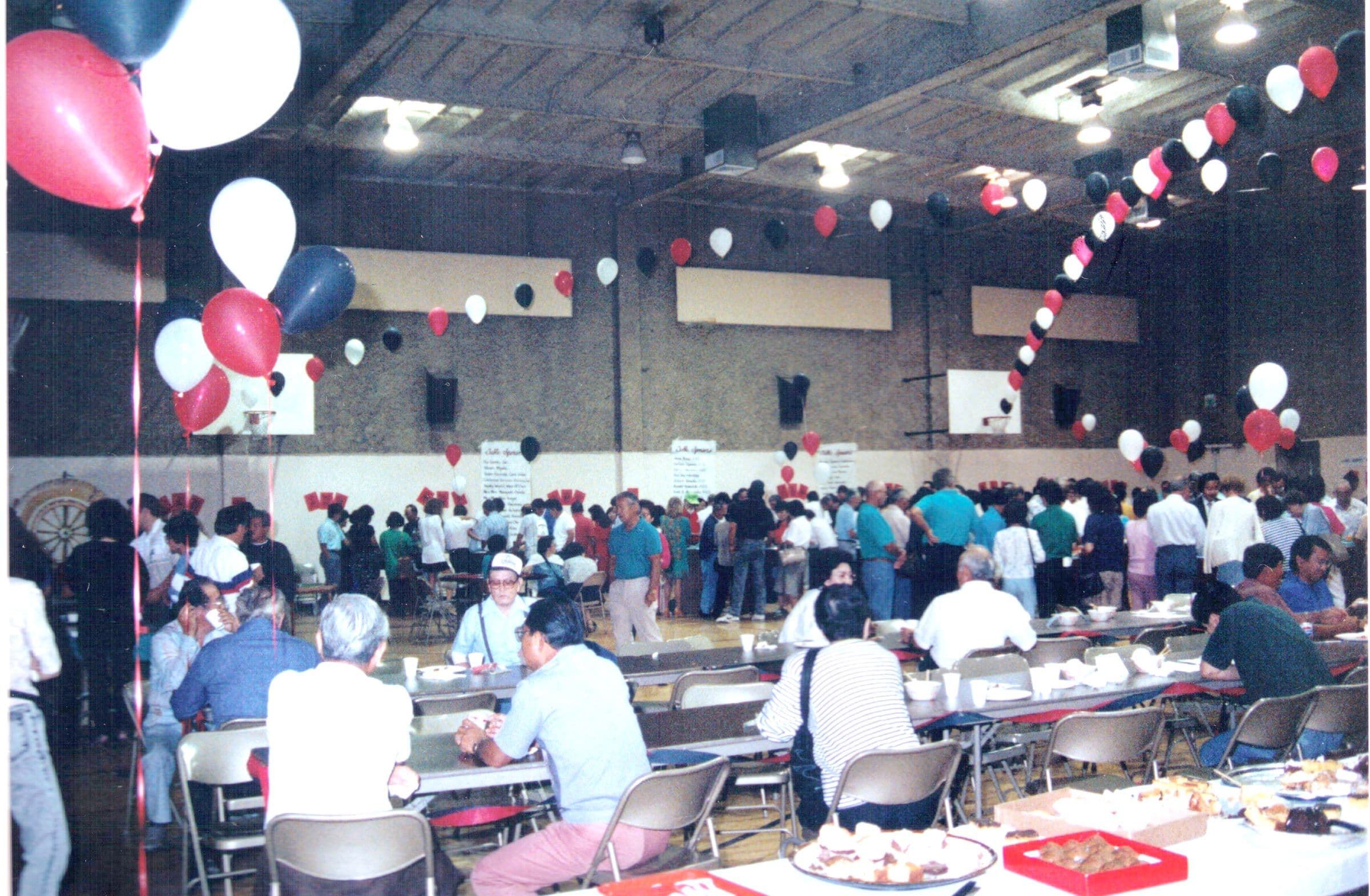 Guests filling long tables in the gym under strings of red, white and black balloons at the 1991 Las Vegas Night