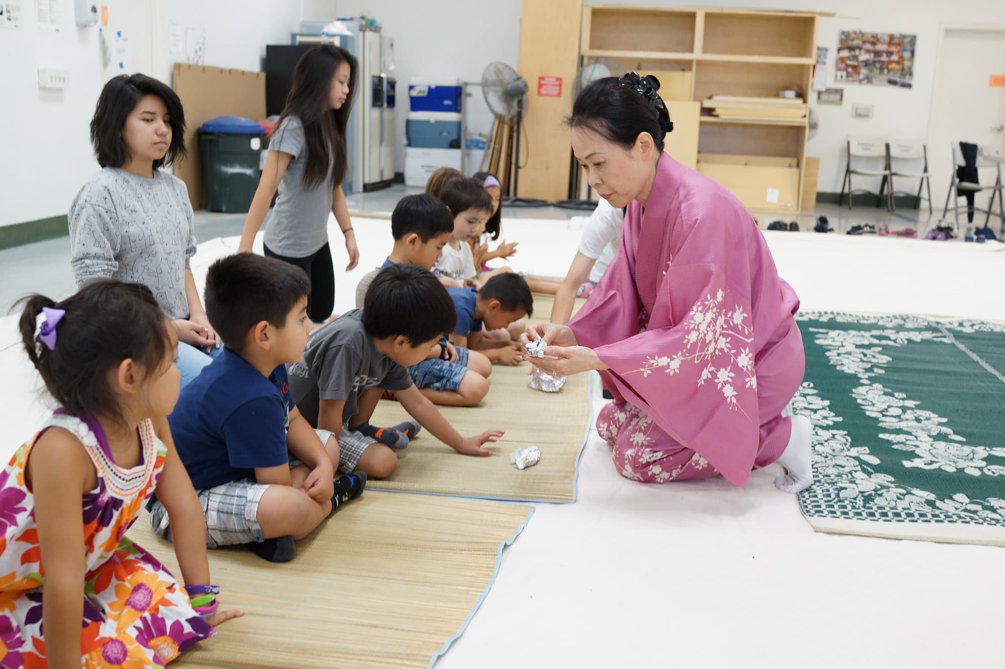 A teacher in a pink kimono showing children how to fold origami