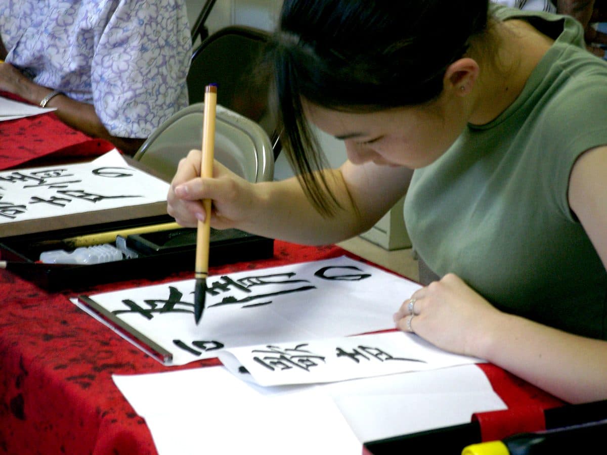 A student writing Japanese characters with a calligraphy brush