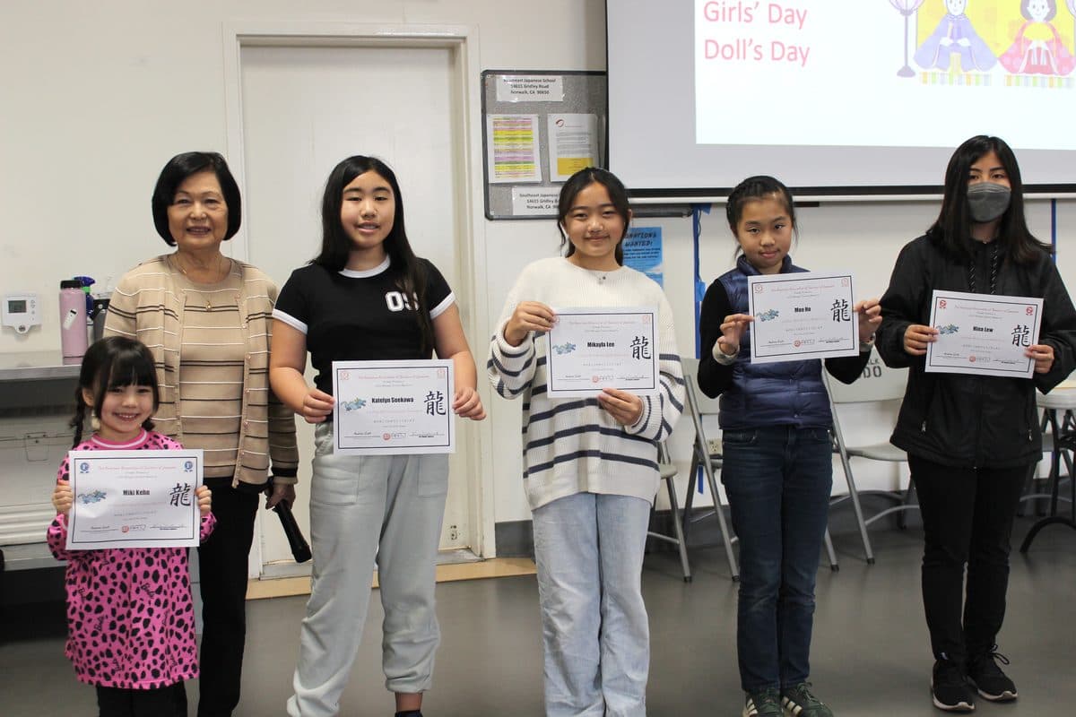 Students holding certificates from the New Year's card contest, with a teacher
