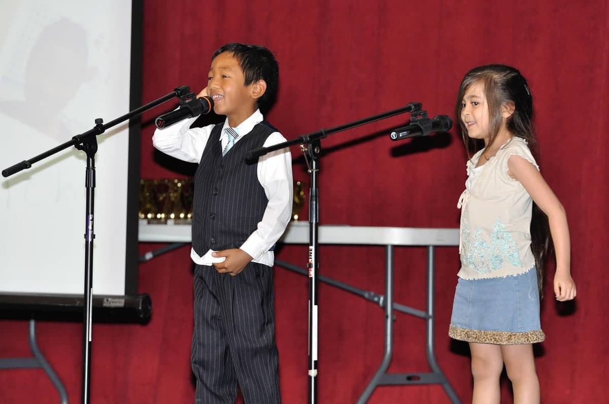 Two young students giving their speeches at microphones on stage